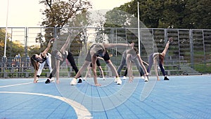 Pleasant slim athletic women doing fitness lunge exercises on the sportground on sunny day in the park