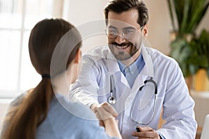 Pleasant smiling male doctor meeting young woman patient at clinic