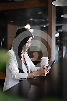 Pleasant woman entrepreneur sitting in office shop and using smartphone.