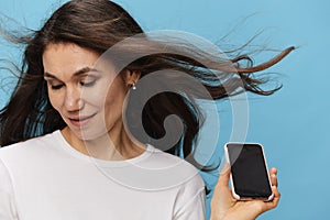 pleasant woman with long hair developing in the wind, in a light T-shirt, holding a fashionable smartphone in her hands