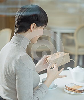 Pleasant woman opening present at table in cafe
