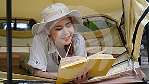 Pleasant woman traveler reading book while lying inside camp tent. Travel, adventure and vacation concept