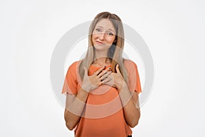 Pleasant young blond woman hold hands on heart thanking for compliments or praises. Studio shot, white background