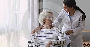 Pleasant young caregiver volunteer medical worker talking to disabled woman.