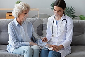 Pleasant young nurse measuring blood pressure of elderly patient.