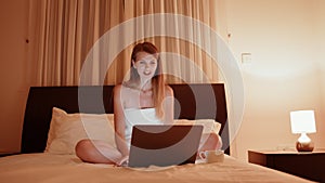 Pleasant young woman smiling and waving hand during video call on modern laptop. Happy lady in bath towel having online