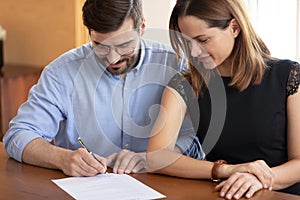 Pleasant young woman watching smiling husband signing contract.