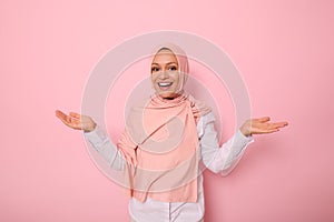 Pleasantly surprised gorgeous Arab muslim woman with covered head in pink hijab joyfully looks at camera smiling beautiful toothy
