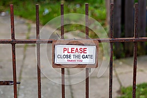 A please close the gate sign hanging on a rusty metal gate