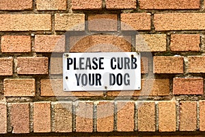 Please Curb Your Dog sign affixed to a brick building wall. Close up photo