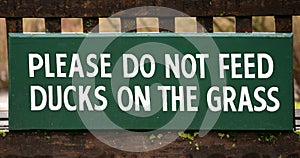 Please Do Not Feed Ducks On The Grass - wooden sign on bench background or banner image