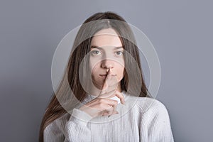 Please dont speak. Mysterious dark hair woman asks to be quiet, presses index finger to lips, demands silence, tells secret