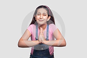 Please forgive or help me. Portrait of sad worry brunette young girl in pink t-shirt and blue denim overalls standing, pleading