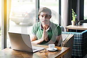 Please forgive me or help! Young worry businessman in green t-shirt sitting and looking at camera and pleading to help or forgive