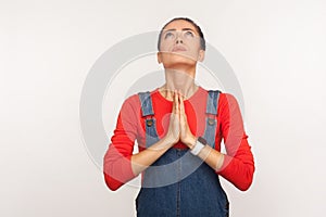 Please god, help! Portrait of imploring worried girl with hair bun in denim overalls looking up and begging, praying