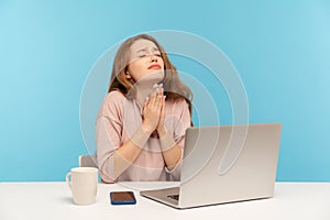 Please, god help! Young woman employee sitting at workplace and keeping eyes closed, praying heartily, pleading