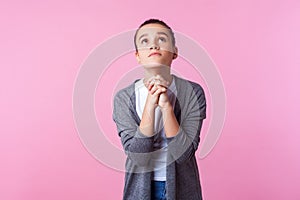 Please God! Portrait of brunette teen girl raising hands in prayer, looking up with hopeful pleading eyes. isolated on pink