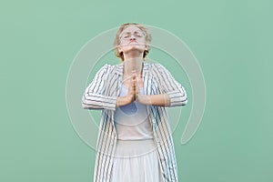 Please help or forgive me. Portrait of hopeful young blonde woman in white striped blouse with eyeglasses standing with palm hands