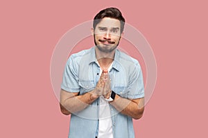 Please help me, or forgive. Portrait of sad hopeful handsome bearded young man in blue casual style shirt standing, looking at