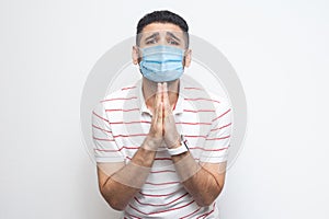 Please help me. Portrait of sad alone man with surgical medical mask in striped t-shirt standing, palm hands and looking at camera