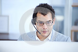 Please hold while I try to find the solution for you. a young call centre agent working on a computer in an office.