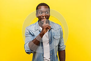 Please, keep silence. Portrait of cheerful handsome man gesturing to be quiet. indoor studio shot isolated on yellow background