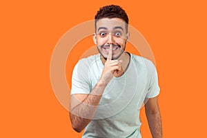 Please, keep silence! Portrait of positive brunette man asking to be quiet. indoor studio shot isolated on orange background