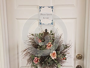 Please knock and wait sign on white door with wreath