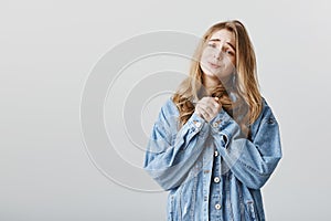 Please, one more offer honey. Portrait of cute european female student with blond hair in denim jacket, clenching hands