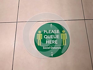 Please queue here. Label on floor of a shop.