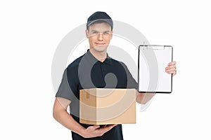 Please sign here to get your box. Cheerful young deliveryman holding carton box and clipboard while isolated on white