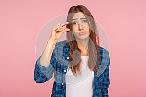 Please, some more. Portrait of cute girl in checkered shirt showing small size or little bit gesture