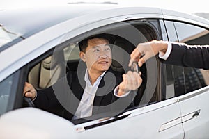 Pleased asian man receiving car keys from male seller