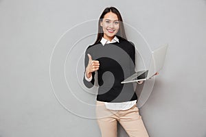 Pleased asian woman in business clothes holding laptop computer