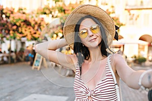 Pleased cute girl wearing trendy yellow sunglasses spending time near outdoor restaurant waiting friends and making