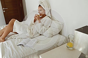 Pleased european girl drink lemonade on bed