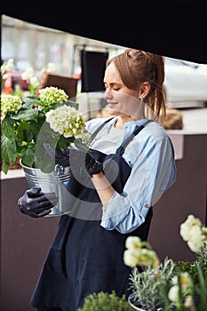 Pleased florist viewing potted flowers in her hands