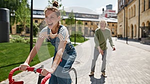 Pleased girl ride bicycle before blurred boyfriend