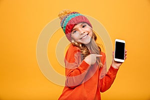 Pleased girl in sweater and hat showing blank smartphone screen