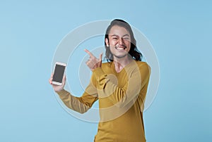 Pleased happy young asian man showing screen smartphone and pointing at copy space on blue backgroung