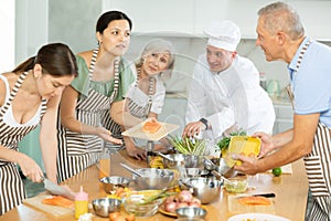Pleased middle-aged woman attendee of cooking course demonstrating piece of salmon on cutting board