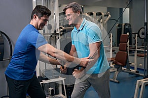 Pleased muscular man doing strength training with fitness coach