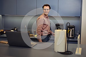 Pleased office employee making himself caffeinated beverage in kitchen