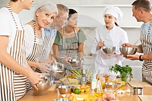 Pleased old woman attendee of cooking course learning how to mix sauce