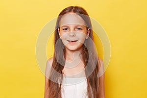 Pleased pretty smiling happy little girl with ponytails standing isolated over yellow background looking at camera with positive