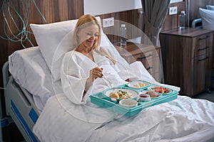 Pleased recumbent patient is having lunch in private clinic ward