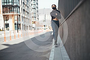 Pleased runner with cornrows jogging along the city street