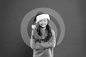 So pleased. time for christmas holiday. small girl in santa hat. cheerful child red background. winter kid fashion