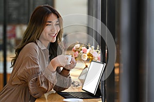 Pleased woman holding coffee cup and looking out of window of coffee shop.