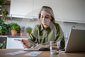 Pleased woman manage household expenses, sit at home table, calculation of family budget in notebook